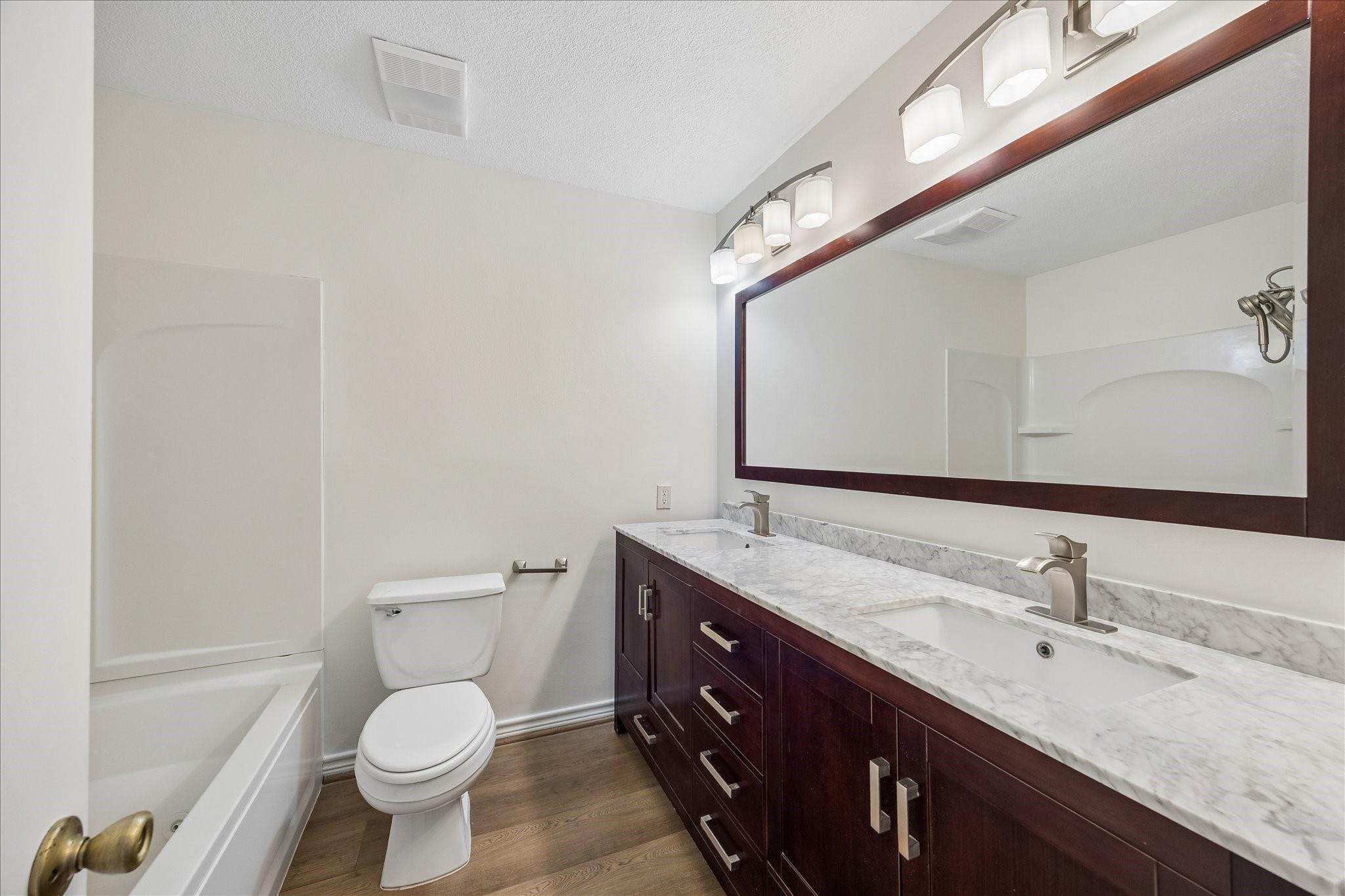 Bathroom with a dark wood double vanity, marble-look counter, and white bathtub.