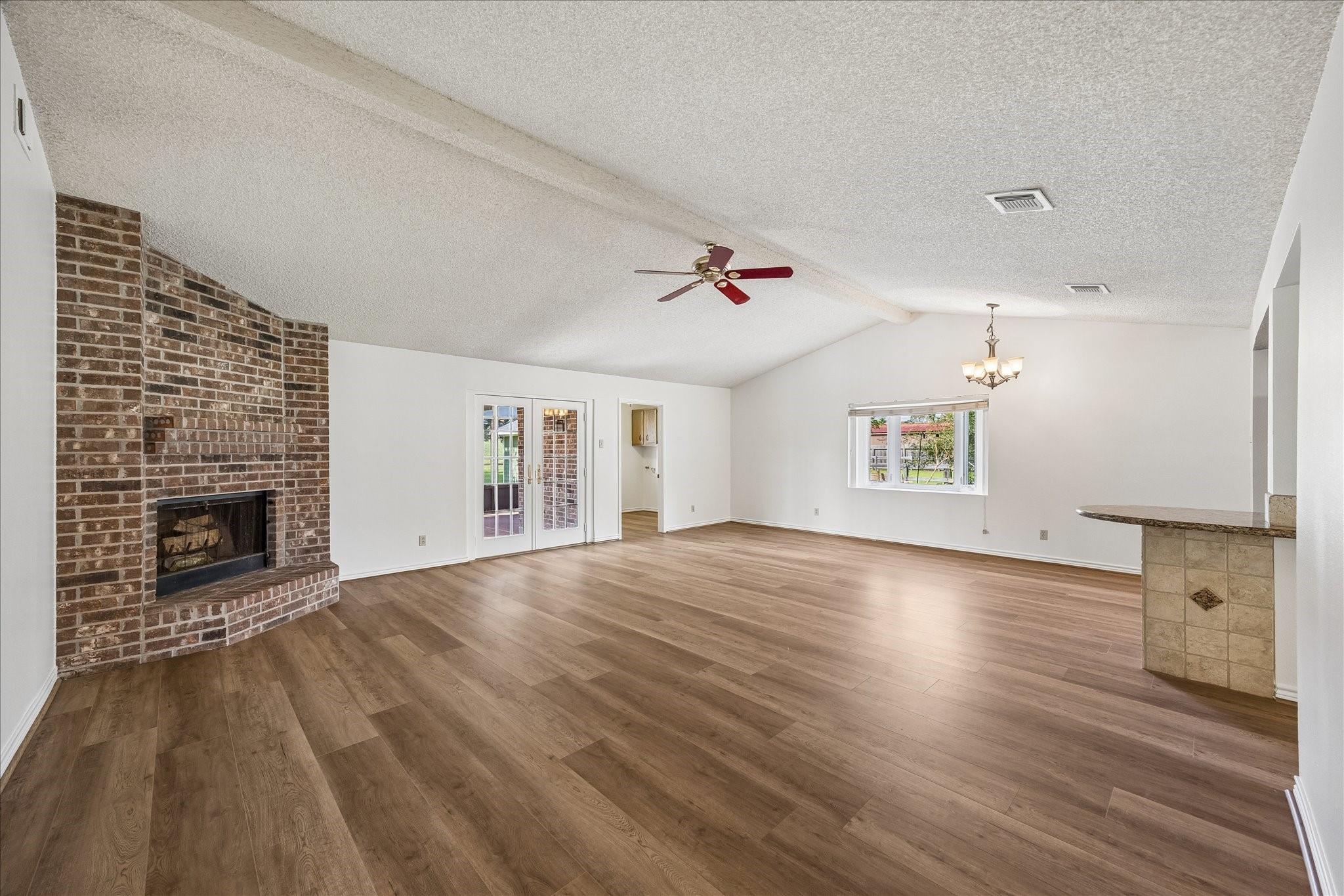 Vacant living and dining area with wood-look floors, a brick fireplace, and French doors to a patio.
