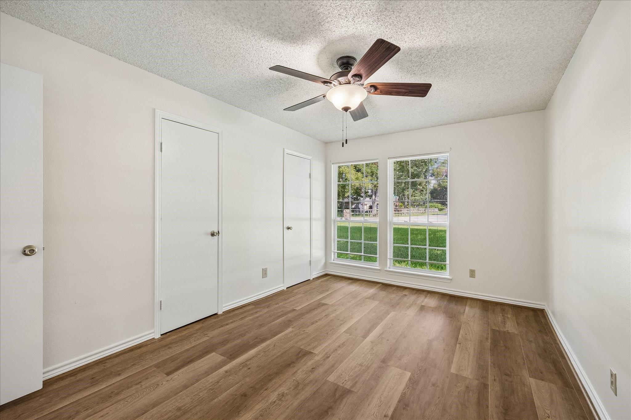 Empty bedroom with wood-look floors, two windows, and a ceiling fan with its light on.