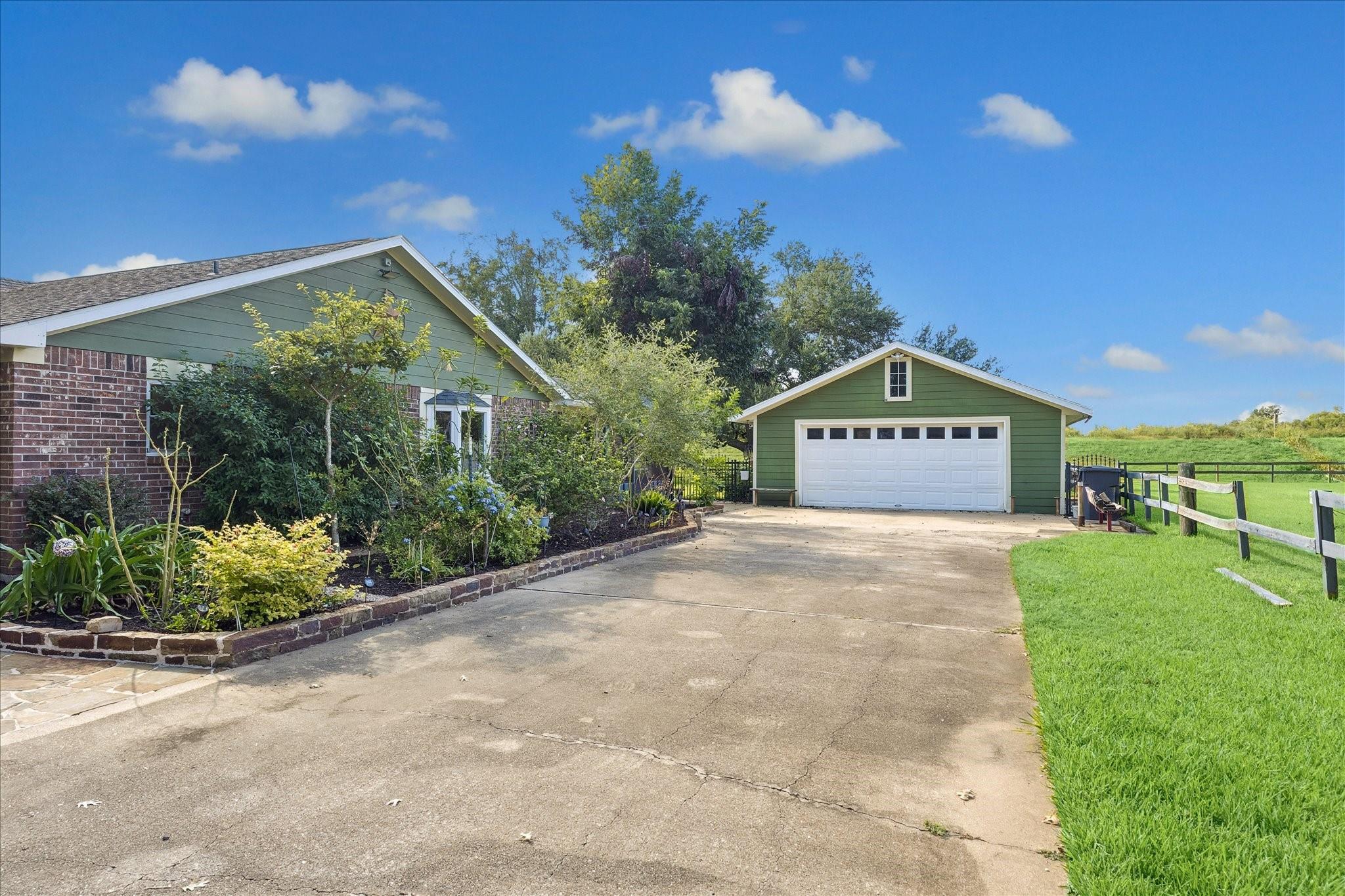 Home and detached green garage beside a wide driveway and landscaped garden.