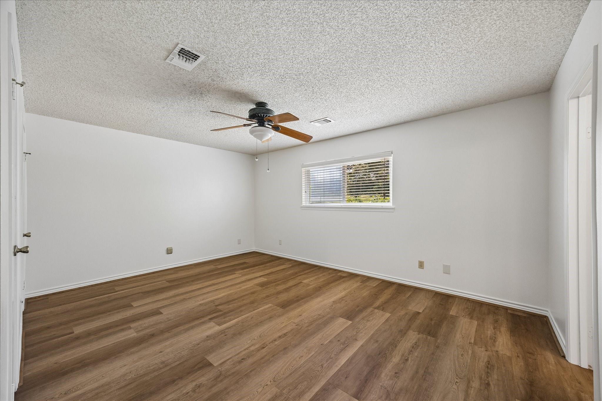 Empty room with wood-look flooring, a ceiling fan, and a window with blinds.