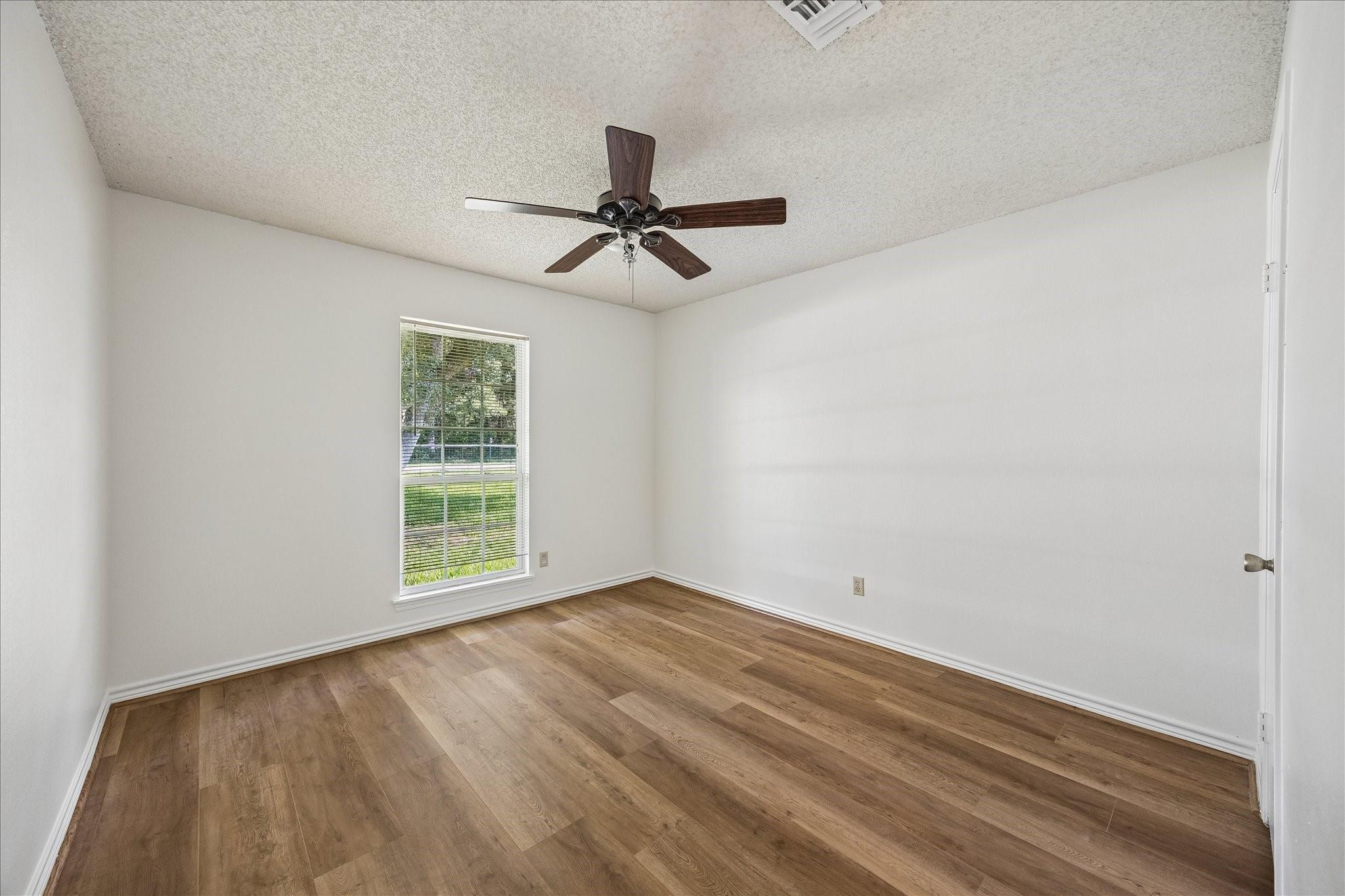 Empty bedroom with wood-look flooring, a ceiling fan, and a window overlooking a green lawn.