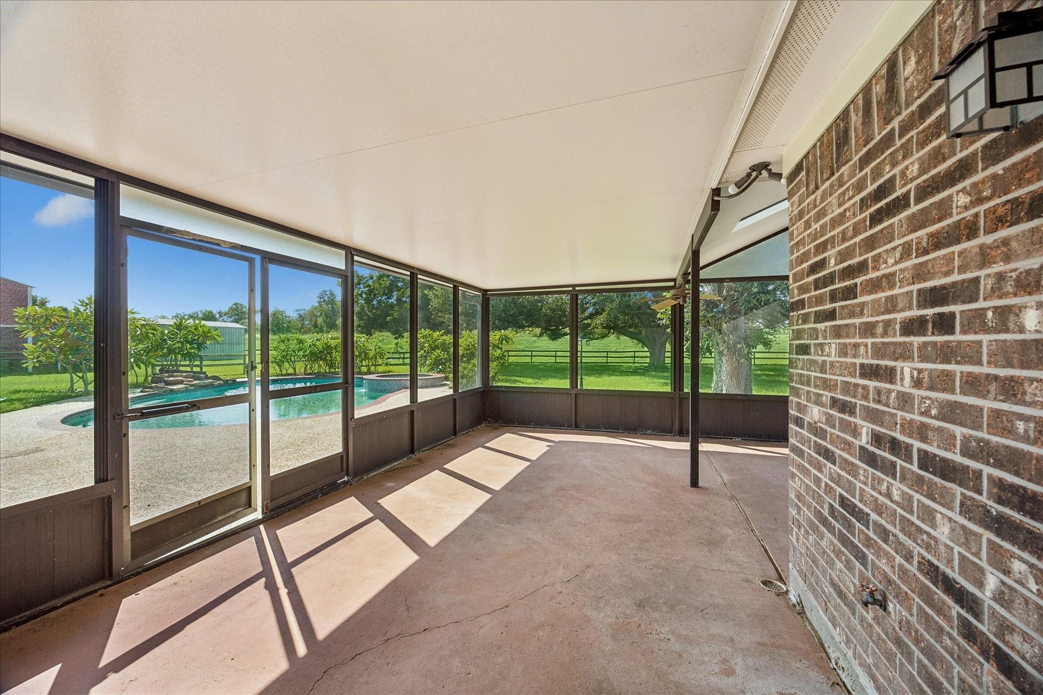 Screened patio overlooking a swimming pool and fenced green yard.