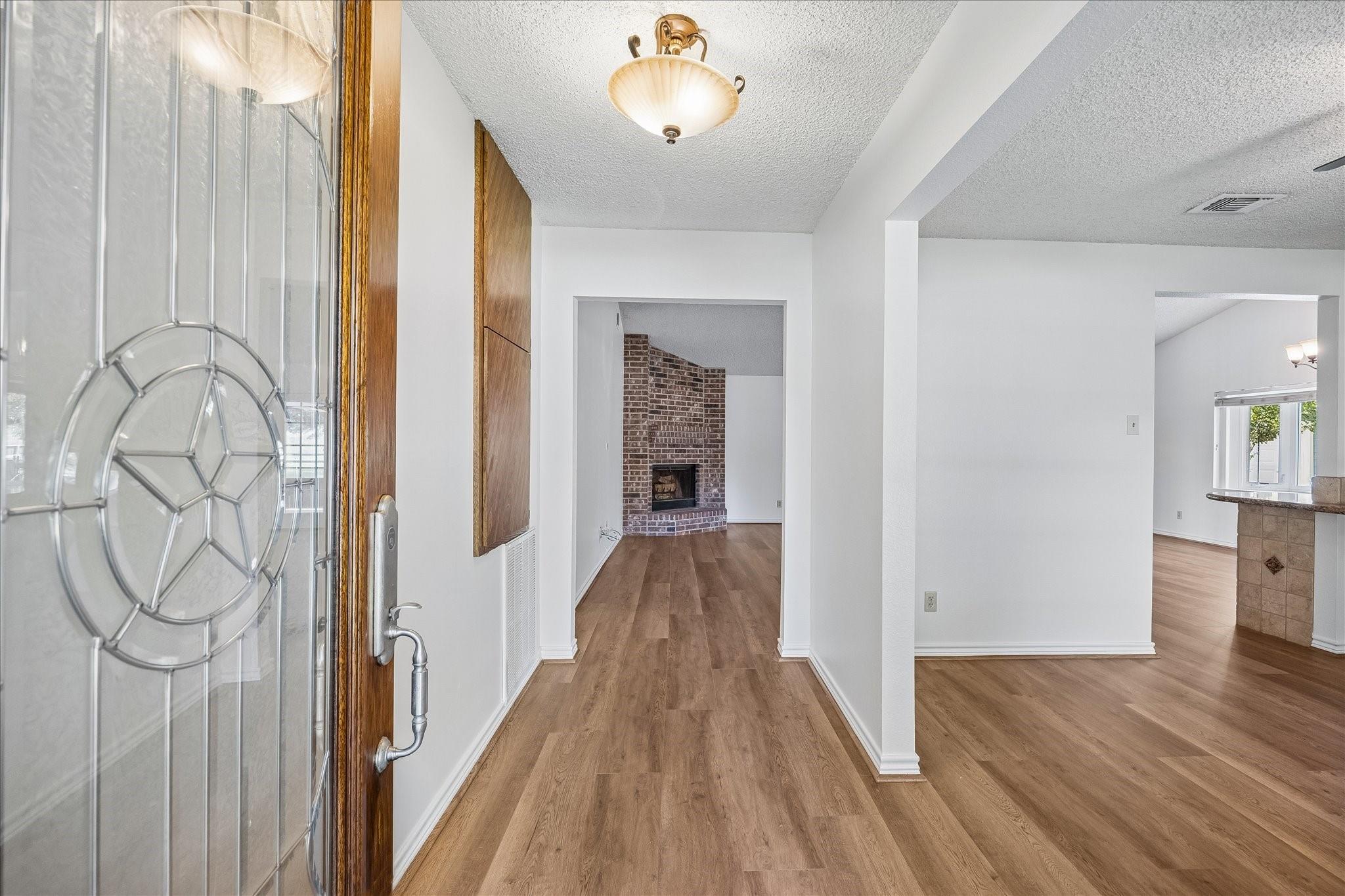 Entry hall with wood-look floors, a glass front door, and a brick fireplace beyond.