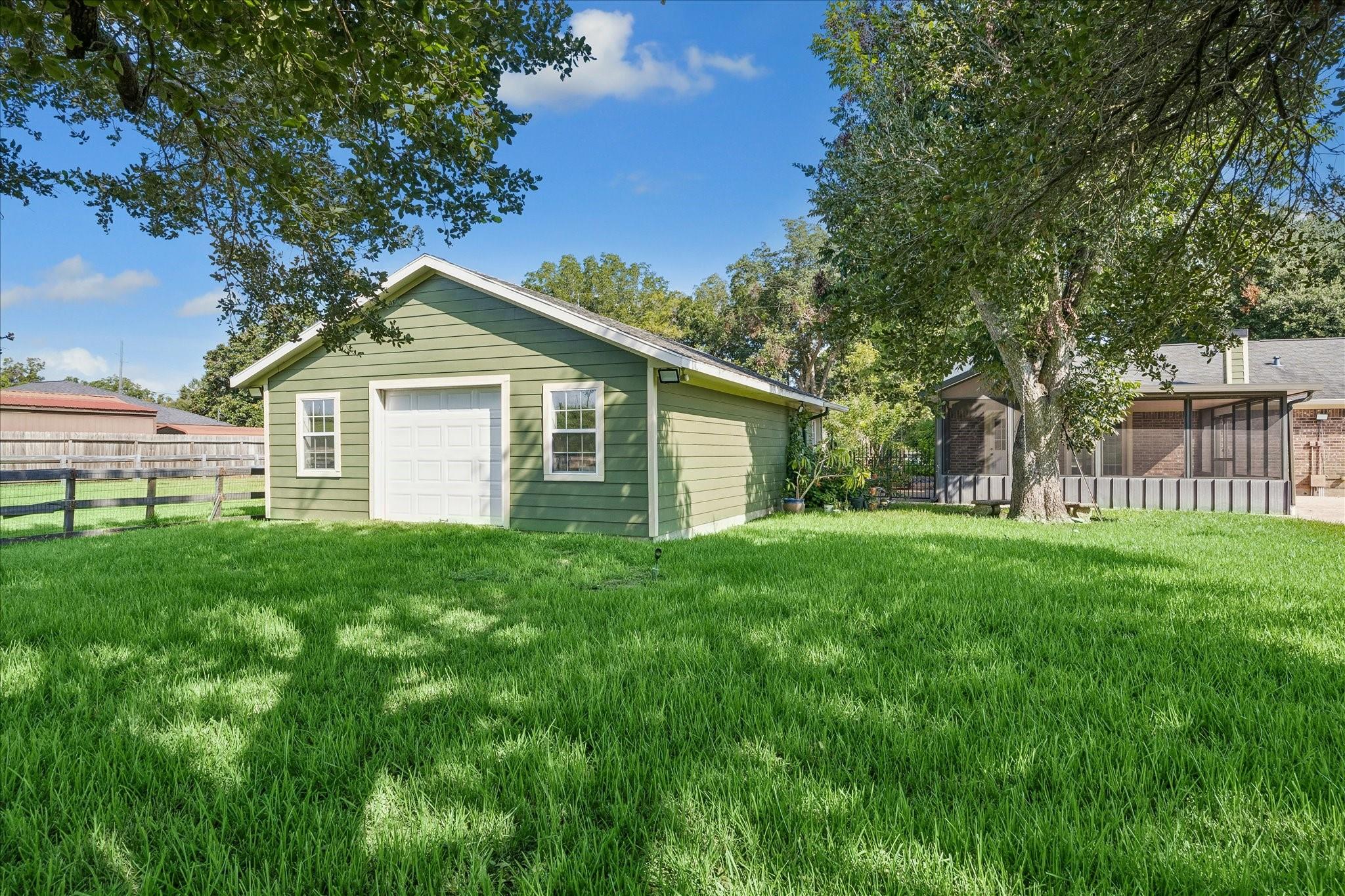Green detached garage with white trim on a grassy lawn beside a screened patio and mature trees.