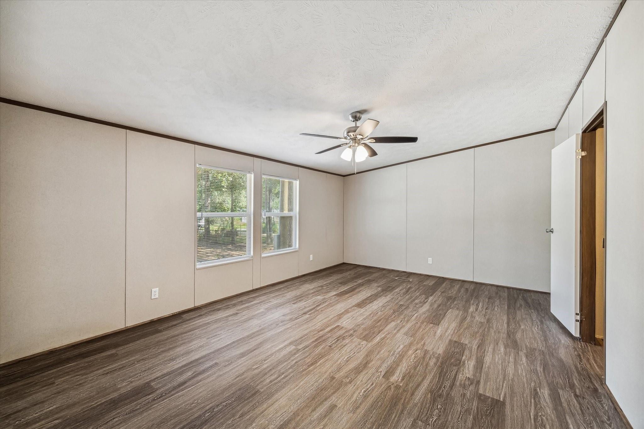 Empty room with wood-look flooring, two windows, and a ceiling fan with lights.