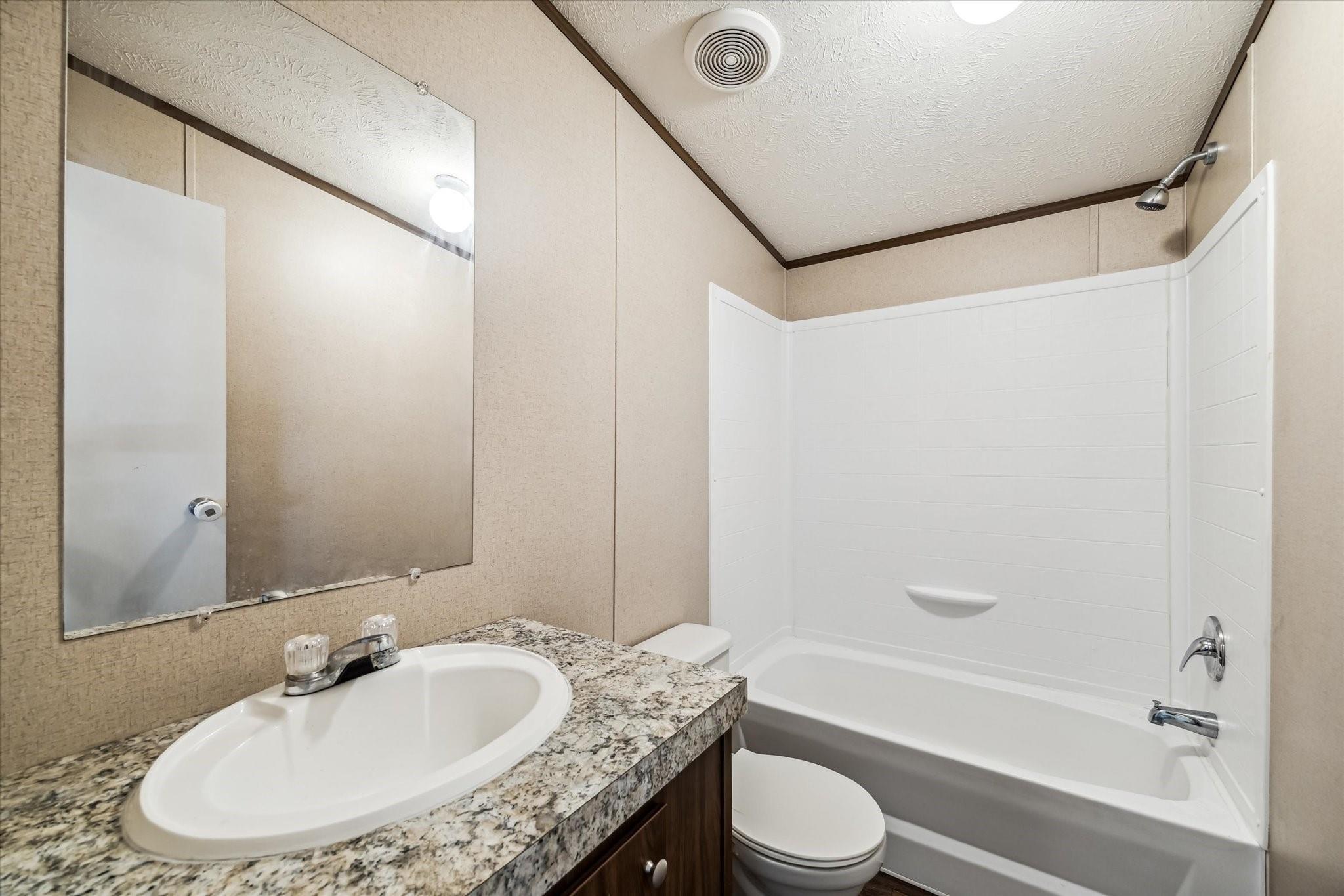 Bathroom with a white tub and shower, toilet, and granite vanity with an oval sink.