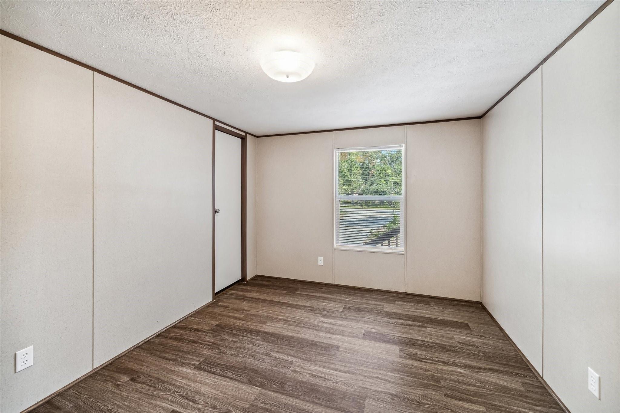 Vacant room with dark wood-look flooring, beige paneled walls, and a window with blinds.