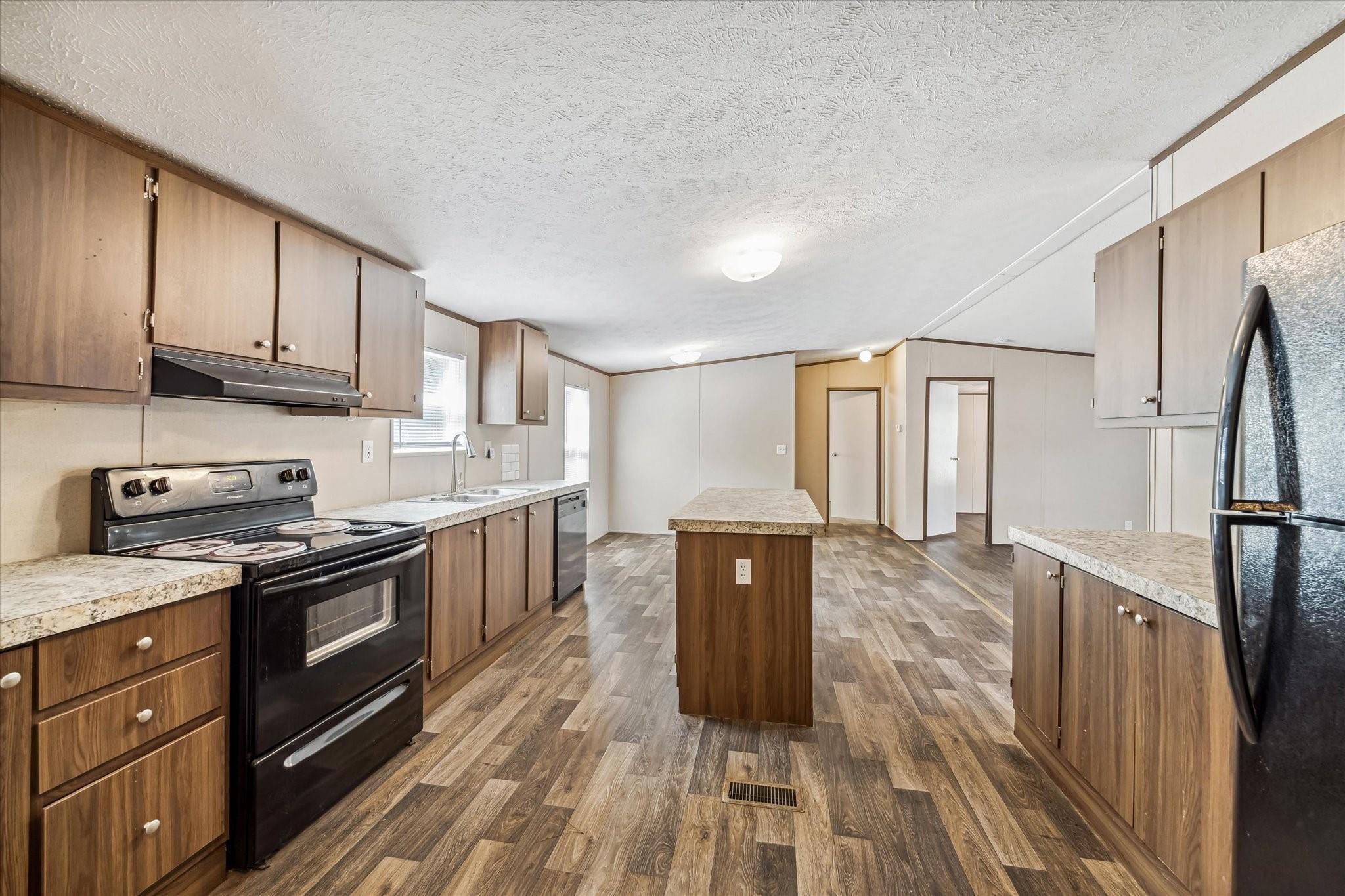 Vacant kitchen with wood-tone cabinets, central island, and wood-look flooring.