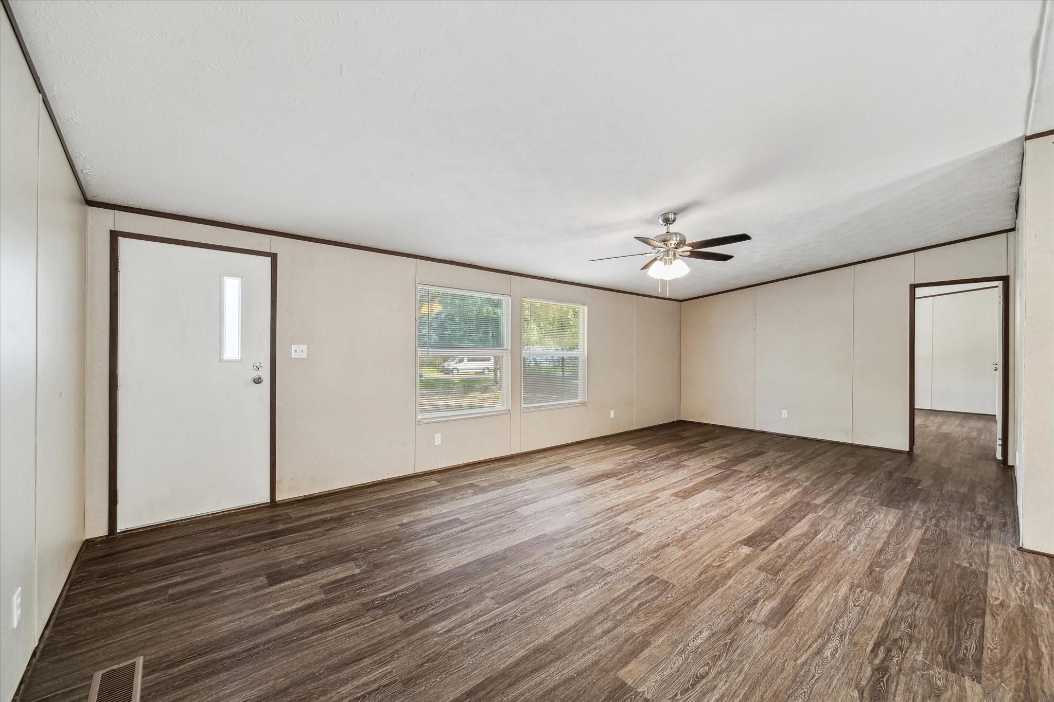 Empty living room with dark plank flooring, two windows, and a ceiling fan with light.