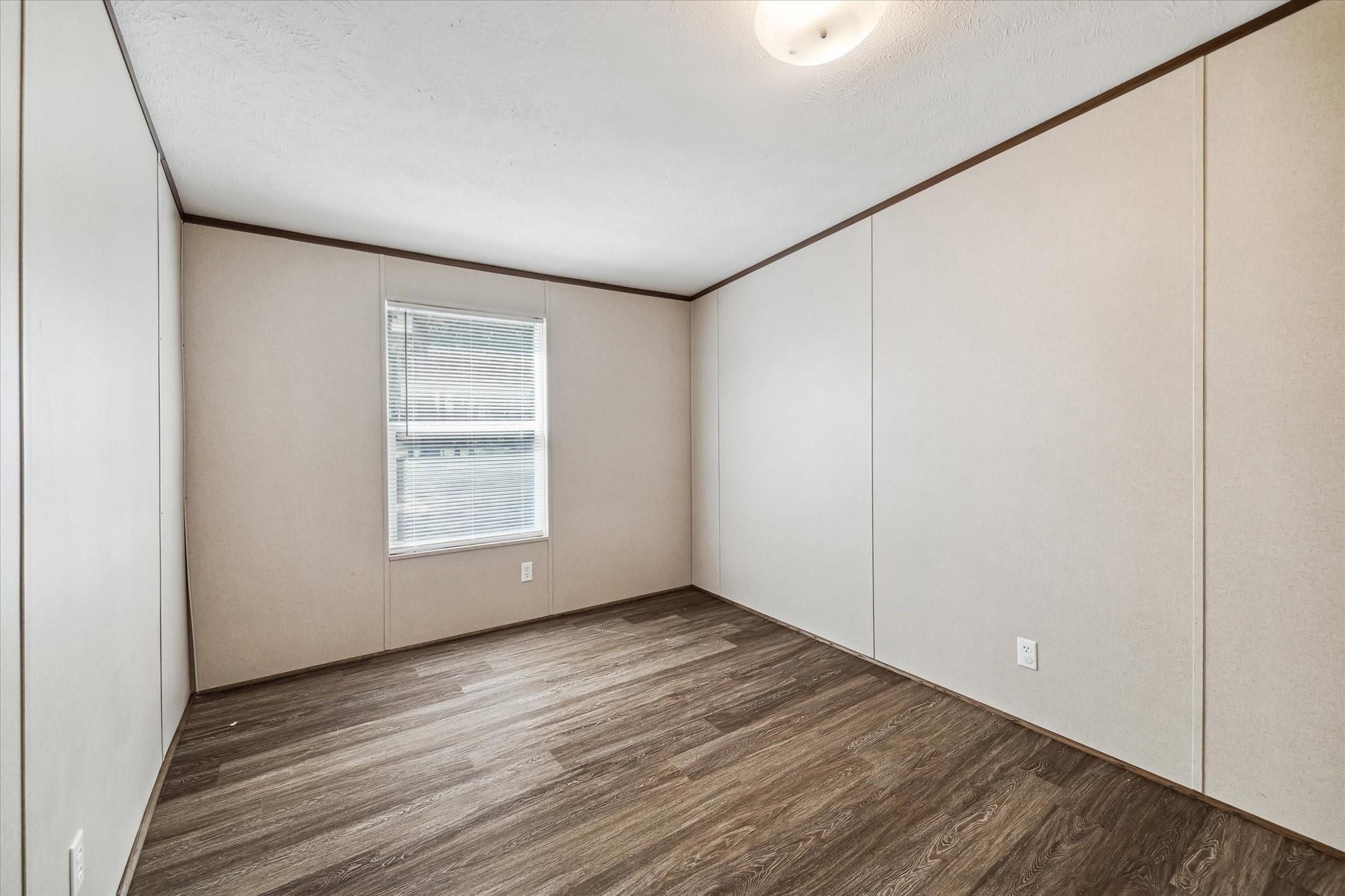 Empty room with beige walls, dark wood-look flooring, and a window with closed blinds.