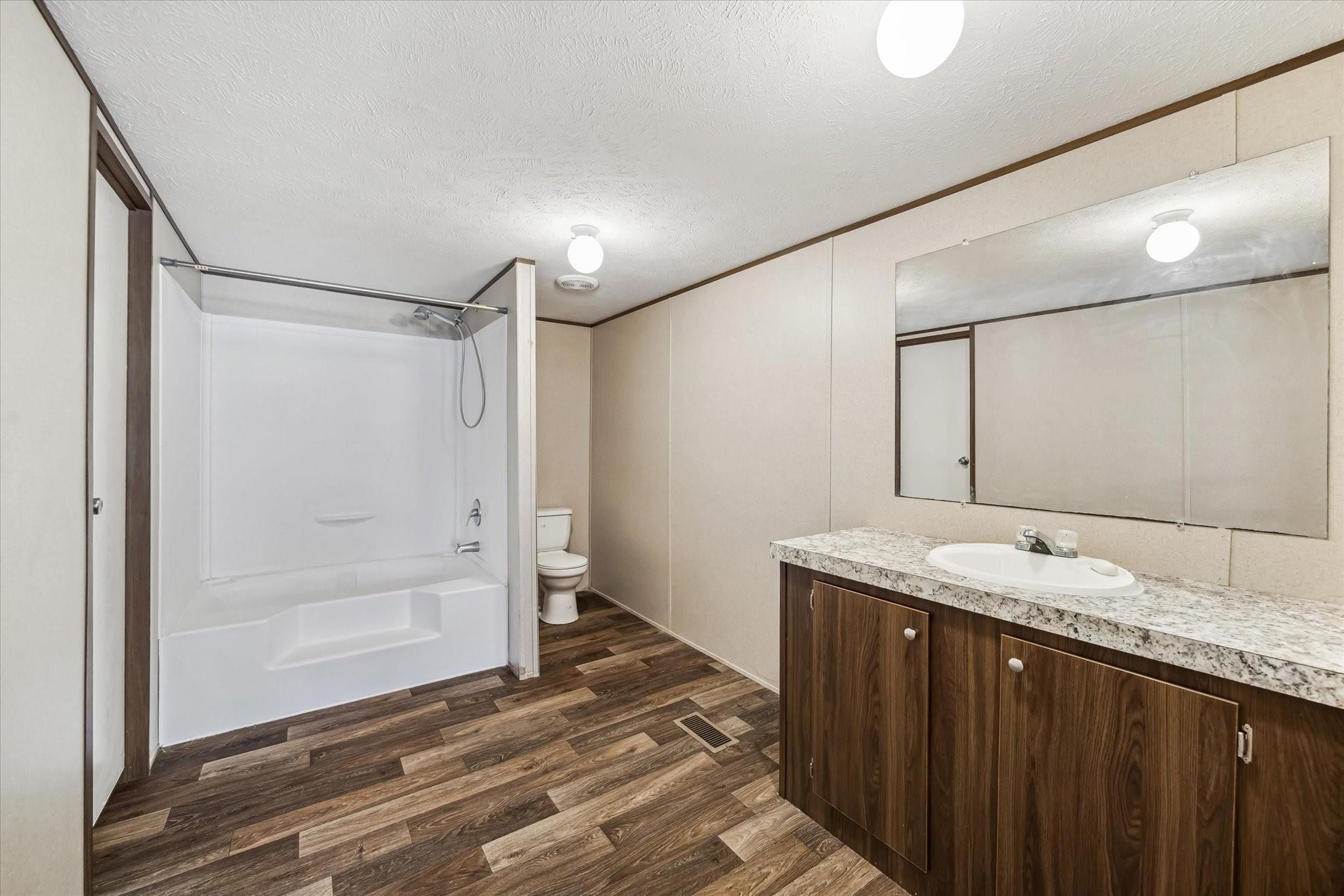 Bathroom with a white tub-shower, toilet, and dark wood vanity beneath a large mirror.