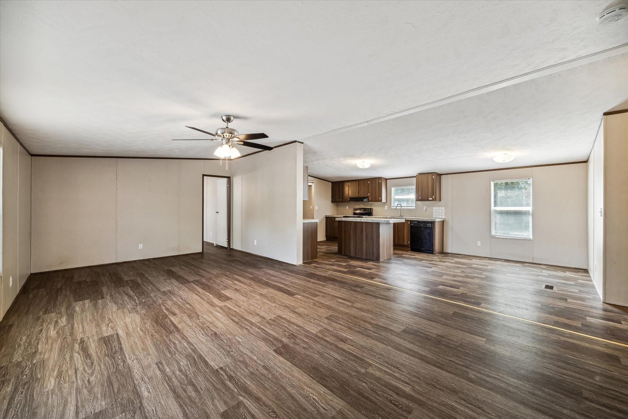 Vacant open-plan living area and kitchen with dark wood-look floors and a kitchen peninsula.