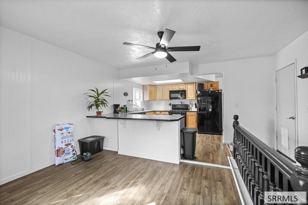 Kitchen with a dark-counter peninsula, light wood cabinets, black appliances, and wood-look flooring.