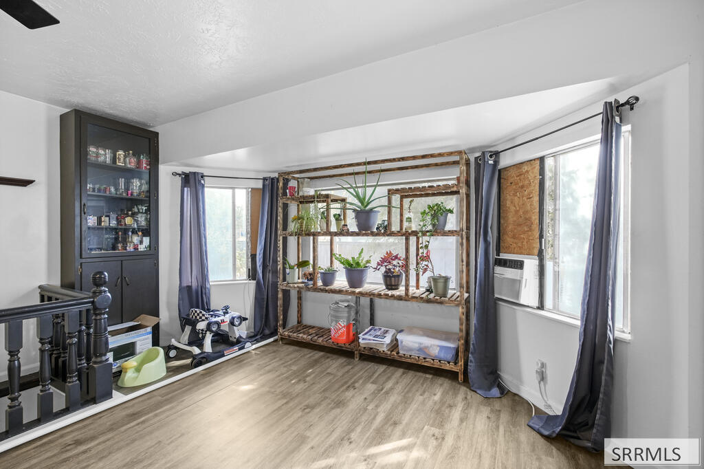 Interior room with rustic plant shelving, two curtained windows, and light wood-look flooring.