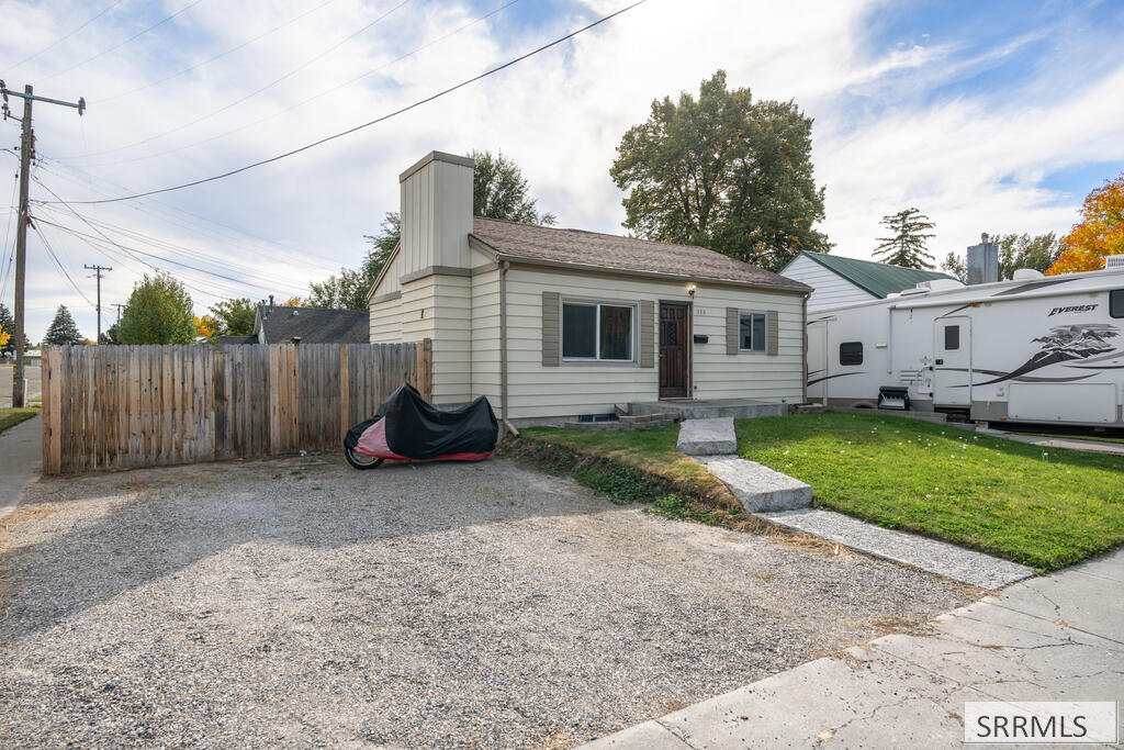 Small cream-sided house with a gravel driveway, wooden fence, and white RV beside it.