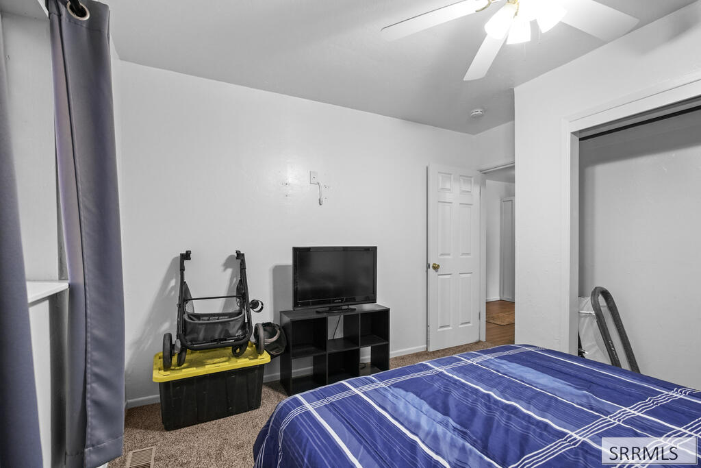 Bedroom with a blue plaid bed, television, and stroller beside a storage bin.