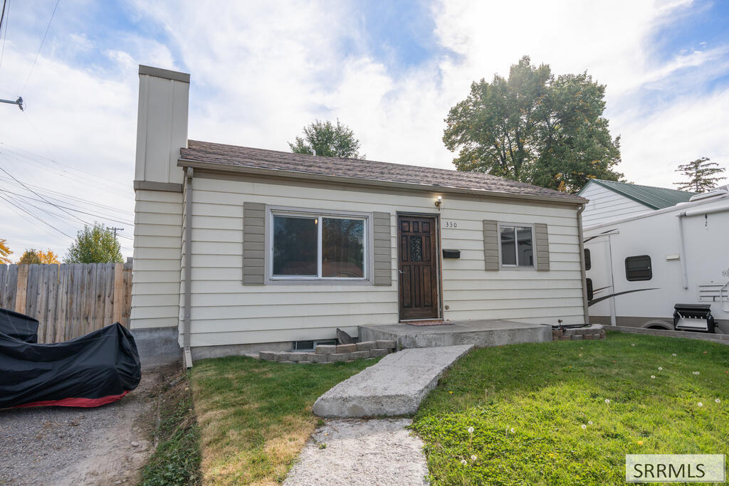 Single-story light-sided house with a tall chimney, front porch, and concrete walkway.