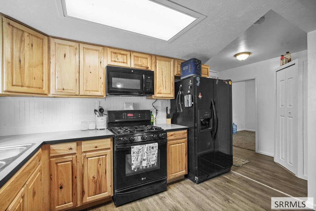 Kitchen with natural-wood cabinets, black appliances, and wood-look flooring.