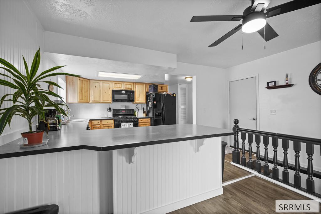Kitchen with honey-toned wood cabinets, black appliances, and a broad gray peninsula counter.