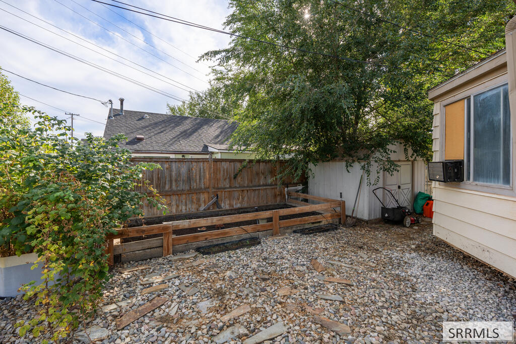 Gravel side yard with raised wooden garden beds, fencing, and mature trees.