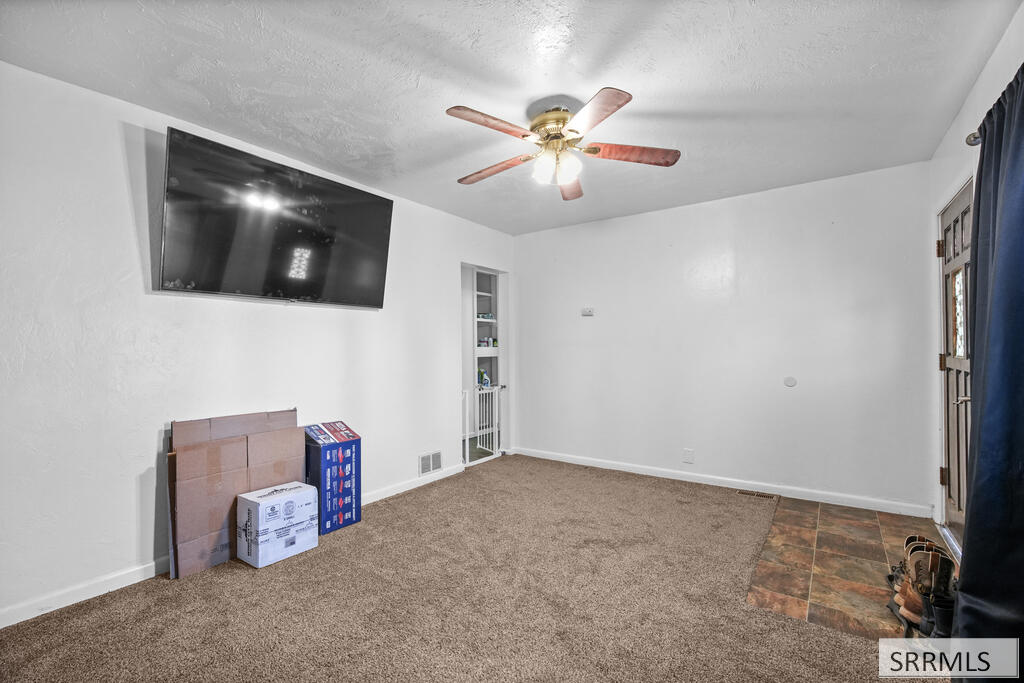 Carpeted room with a wall-mounted television, ceiling fan, and tiled entry area.