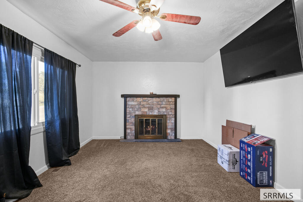 Living room with a stone fireplace, wall-mounted television, blue curtains, and ceiling fan.
