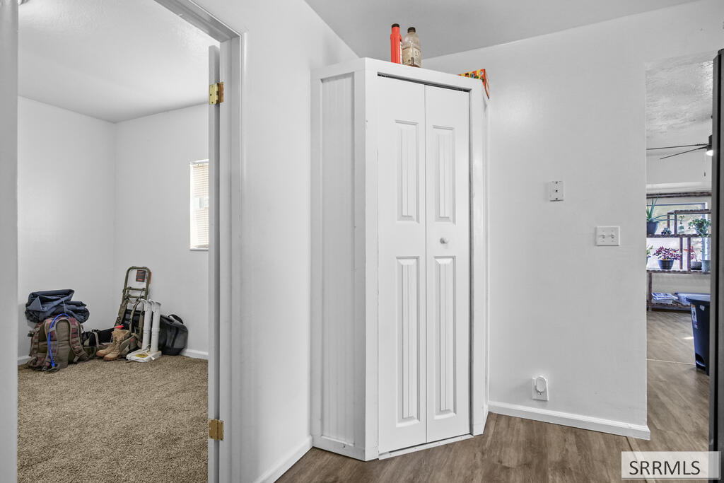 Hallway with a tall white closet, wood-look flooring, and open doorways to adjoining rooms.
