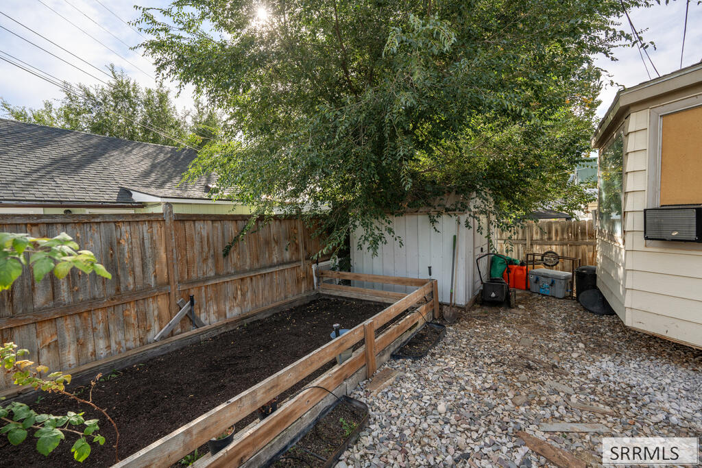 Yard with a raised garden bed beneath a leafy tree and gravel ground cover.