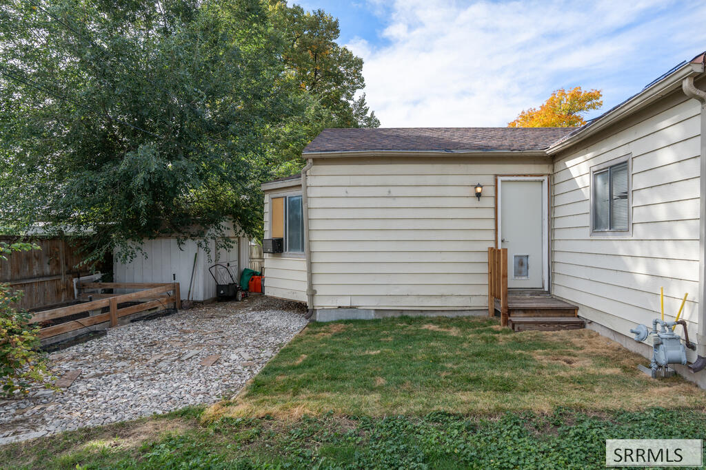 Rear of a light-sided house with back steps, a gravel yard, and mature trees.