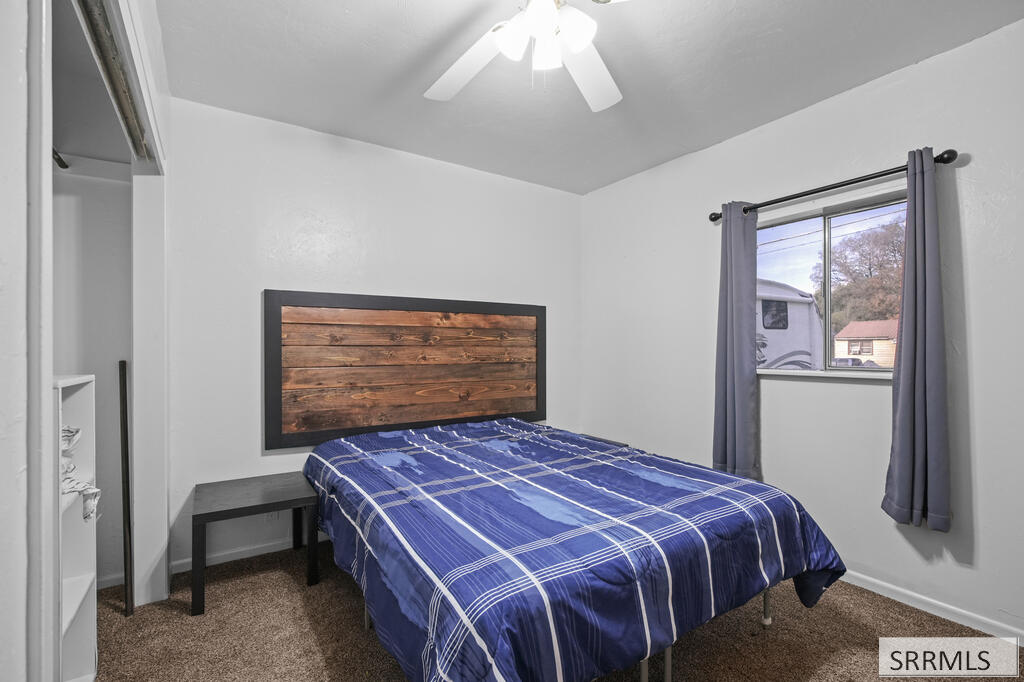 Bedroom with a blue plaid bedspread, wood-plank headboard, and a window overlooking a neighboring yard.