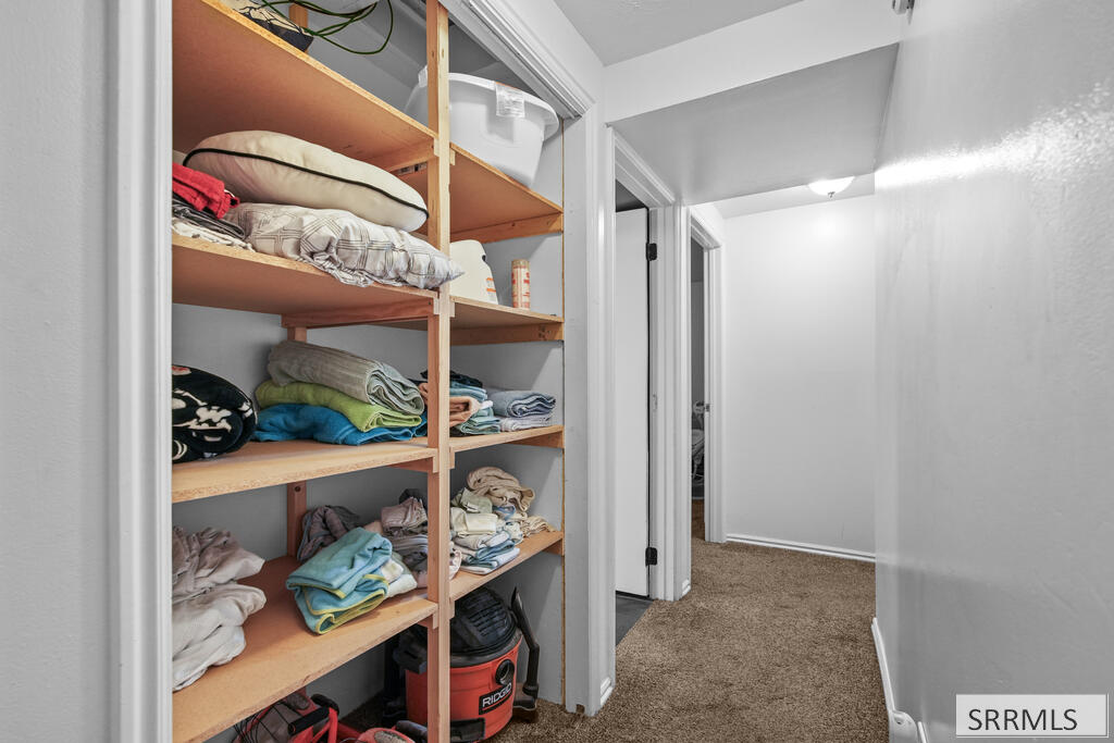 Storage closet with wooden shelves of folded linens beside a carpeted hallway.
