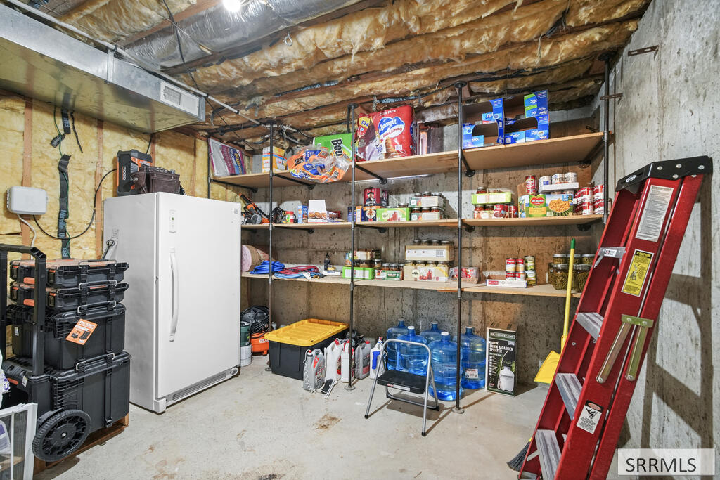 Basement storage room with stocked shelves, a white freezer, water jugs, and a red ladder.