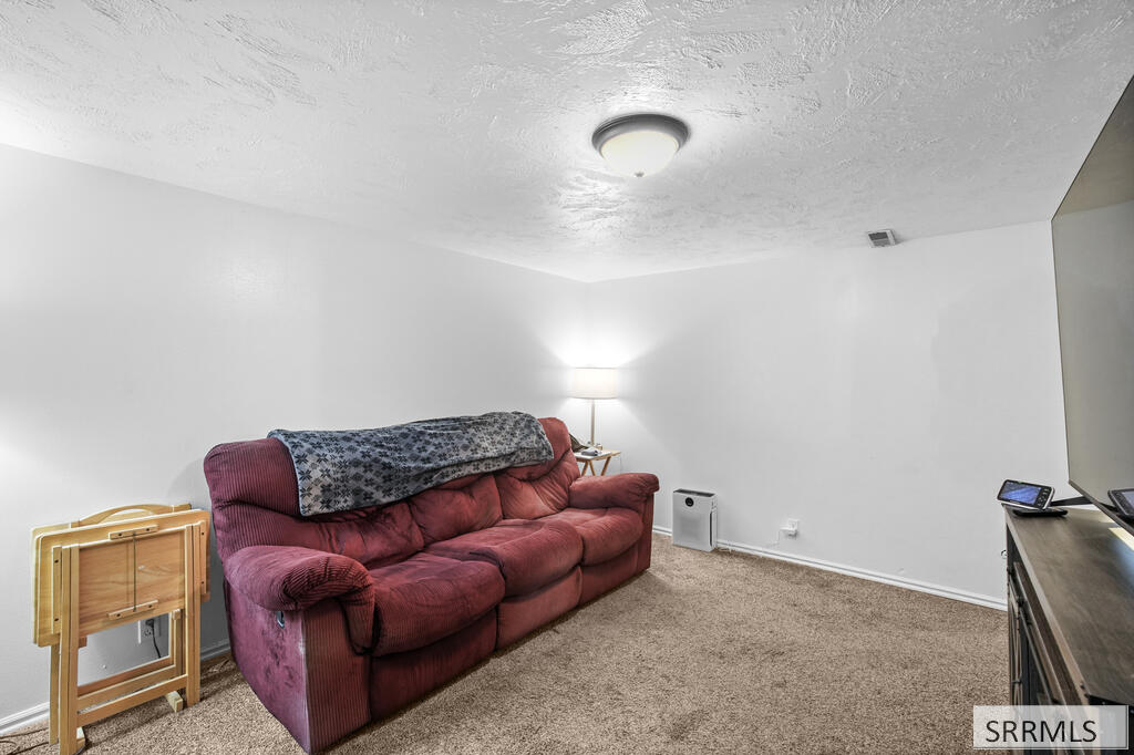 Furnished room with a burgundy sofa, beige carpet, and television stand.