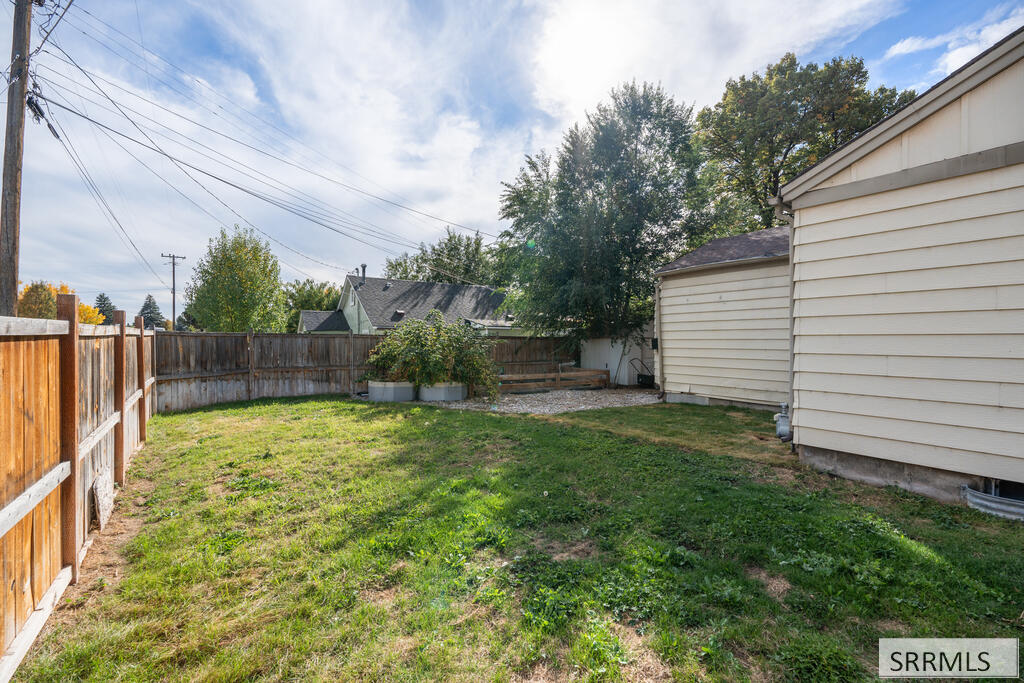 Fenced backyard with a patchy lawn, raised planters, and the side of the house.