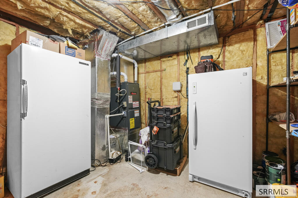Basement utility room with two upright freezers, furnace, exposed insulation, and storage shelving.