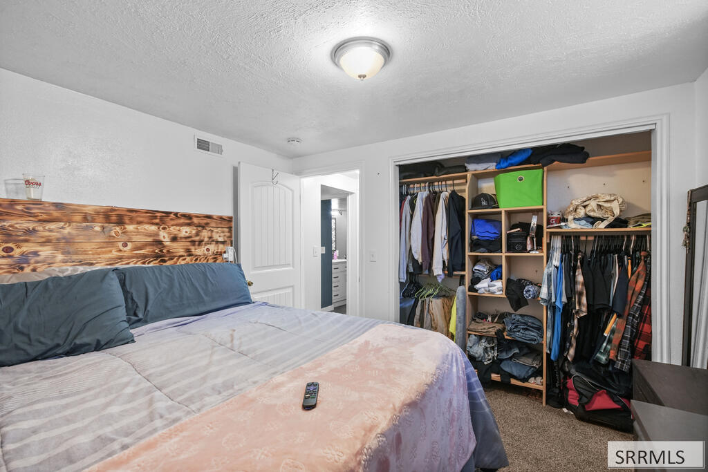 Bedroom with a large bed and an open, clothing-filled closet.