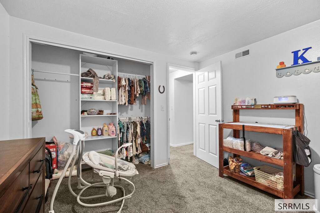 Nursery with an open clothes-filled closet, baby rocker, and wooden changing table.
