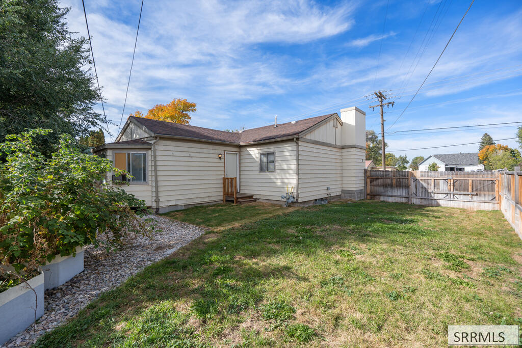 Rear exterior of a single-story home with a fenced grassy yard and gravel path.
