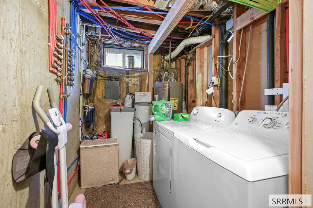 Basement laundry room with white washer and dryer, exposed framing, plumbing, and a small high window.