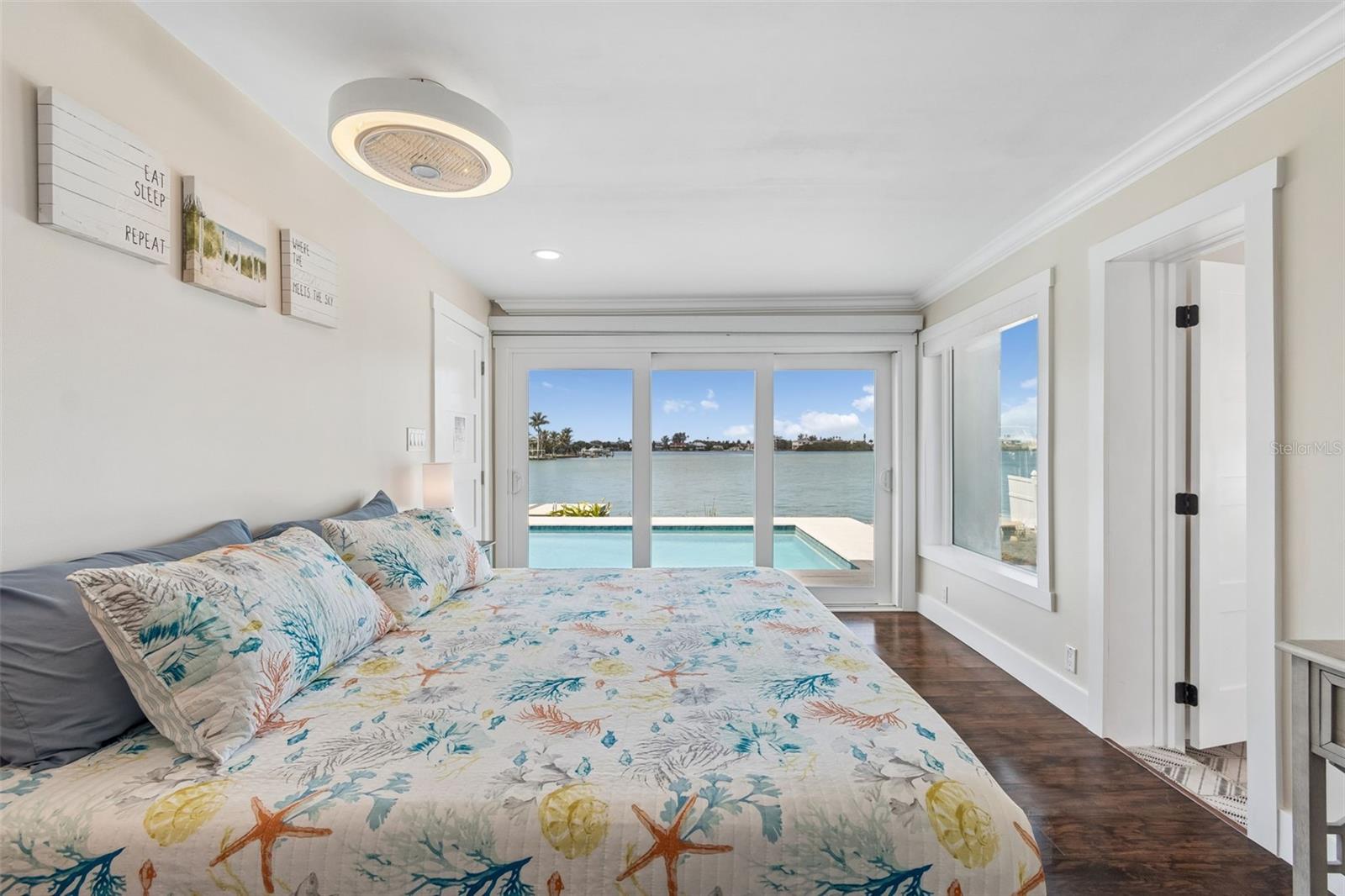 Bedroom with marine-patterned bedding and sliding doors overlooking a pool and waterfront.