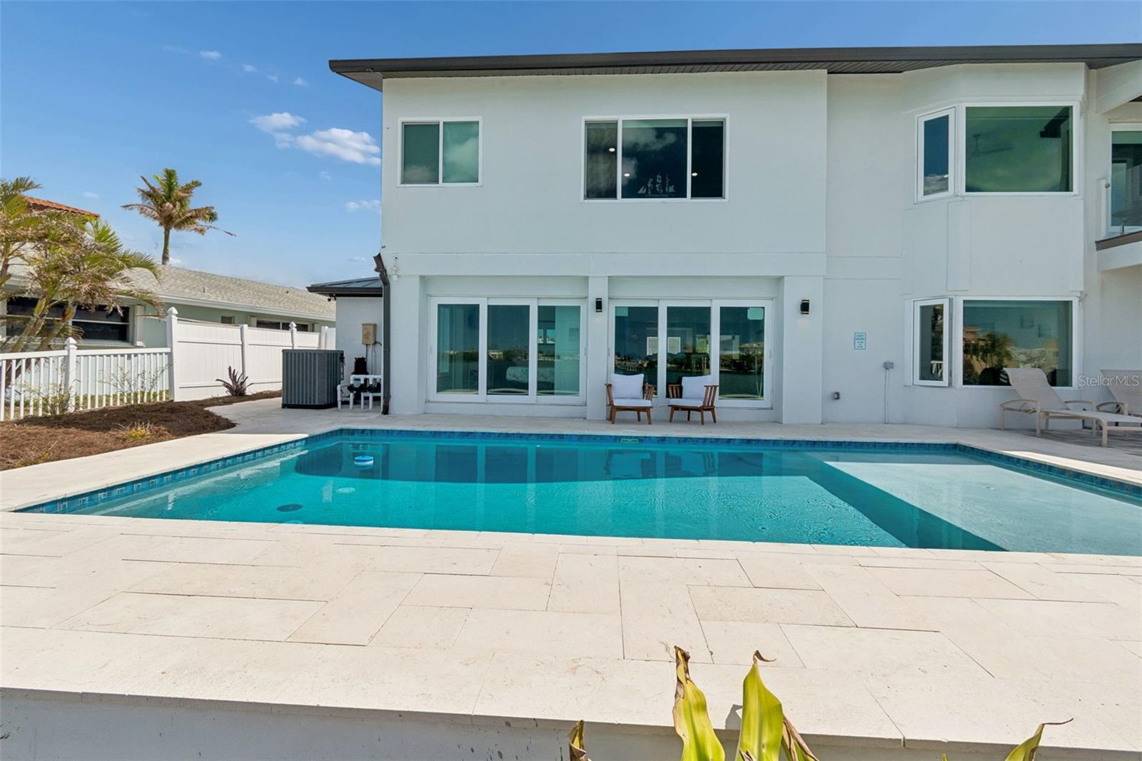 Modern white two-story home behind a swimming pool and pale stone patio.