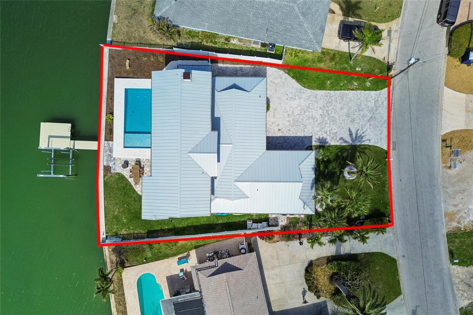 Aerial view of a canal-front home with a backyard pool, private dock, and red property boundary.