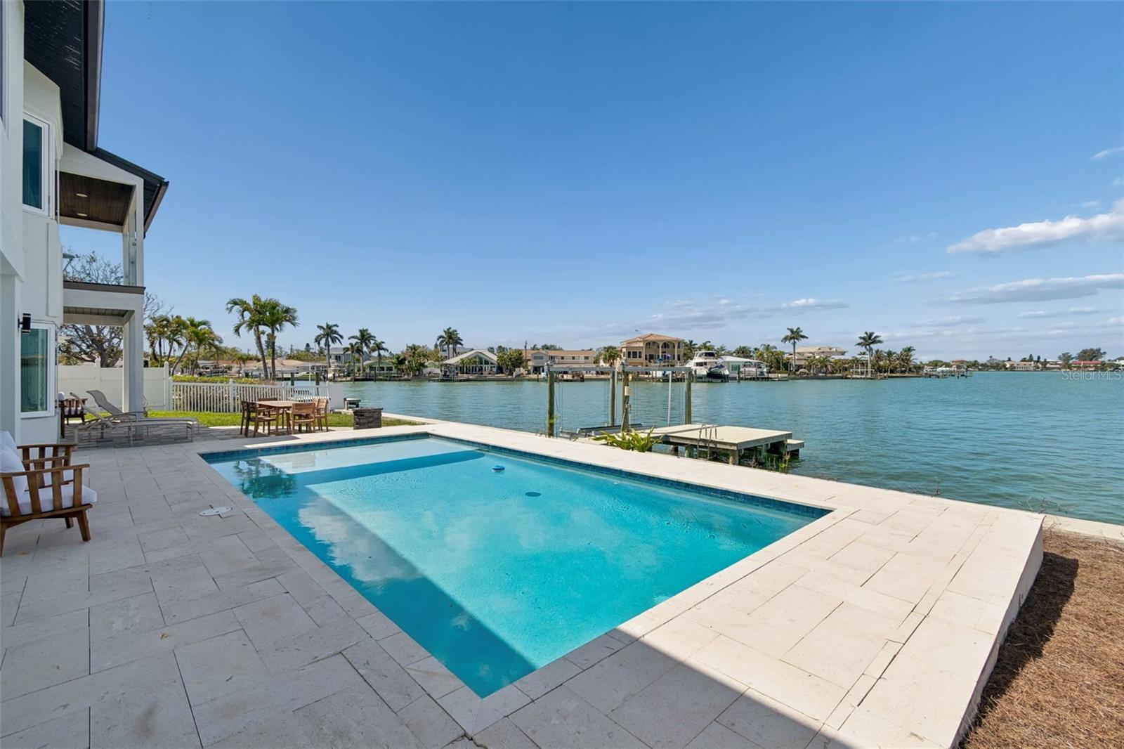 Waterfront backyard pool with a stone patio, private dock, and homes across the water.