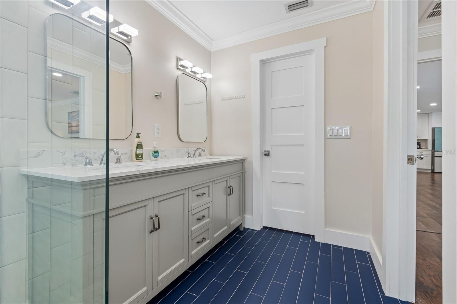Bathroom with gray double vanity, glass shower, and deep blue tile floor.