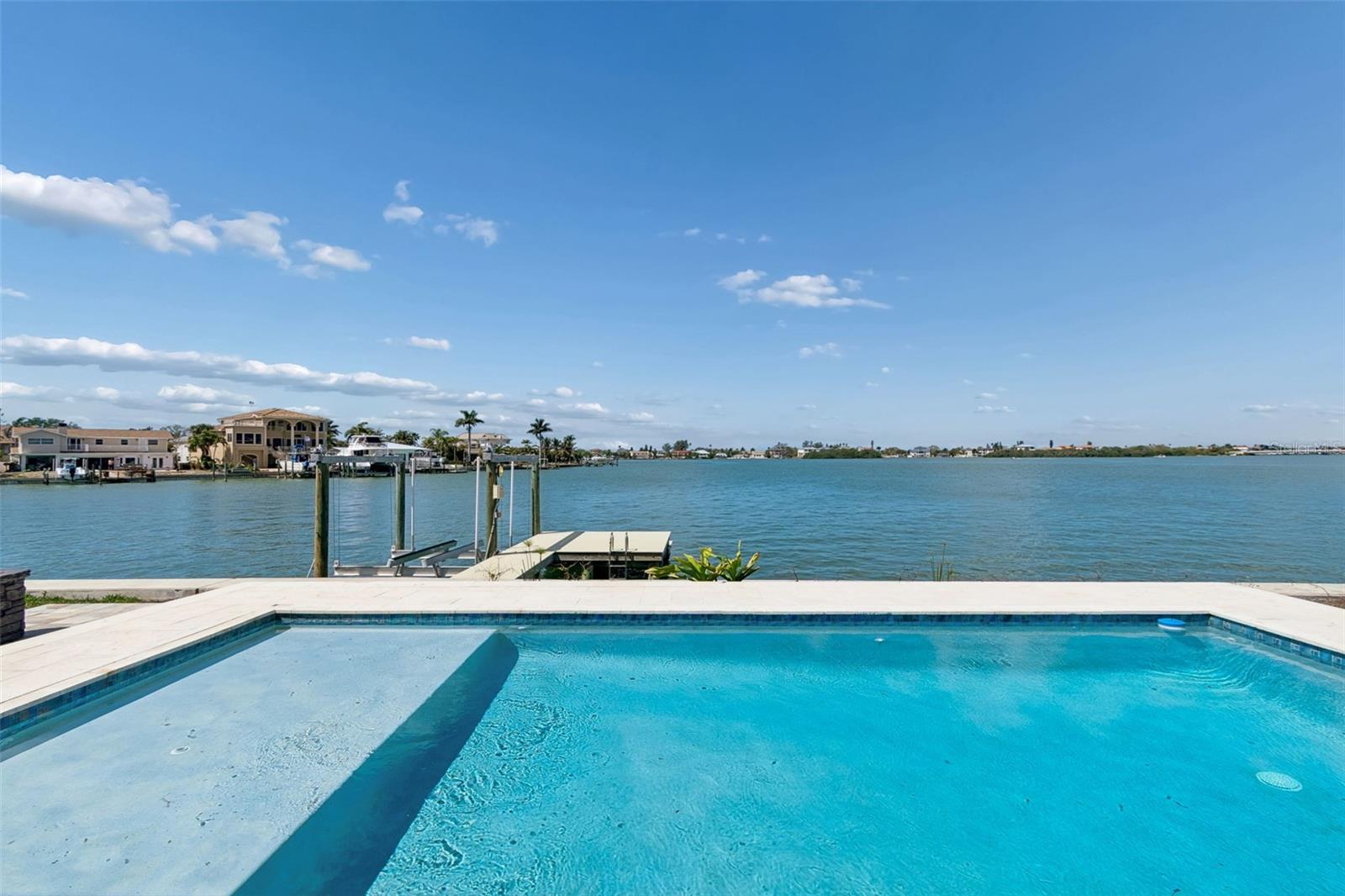 Swimming pool overlooking the water, with a private dock and homes along the opposite shore.
