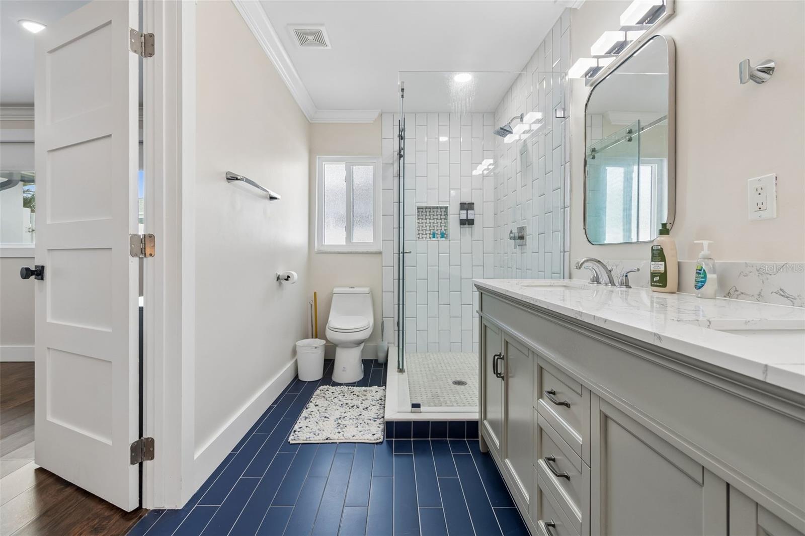 Bathroom with a glass walk-in shower, gray vanity, and dark blue tile floor.