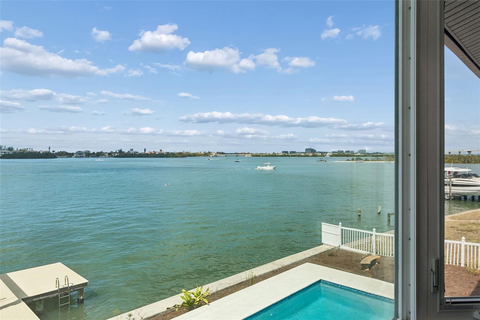 Waterfront view across the bay, with a backyard pool, dock, and boats.