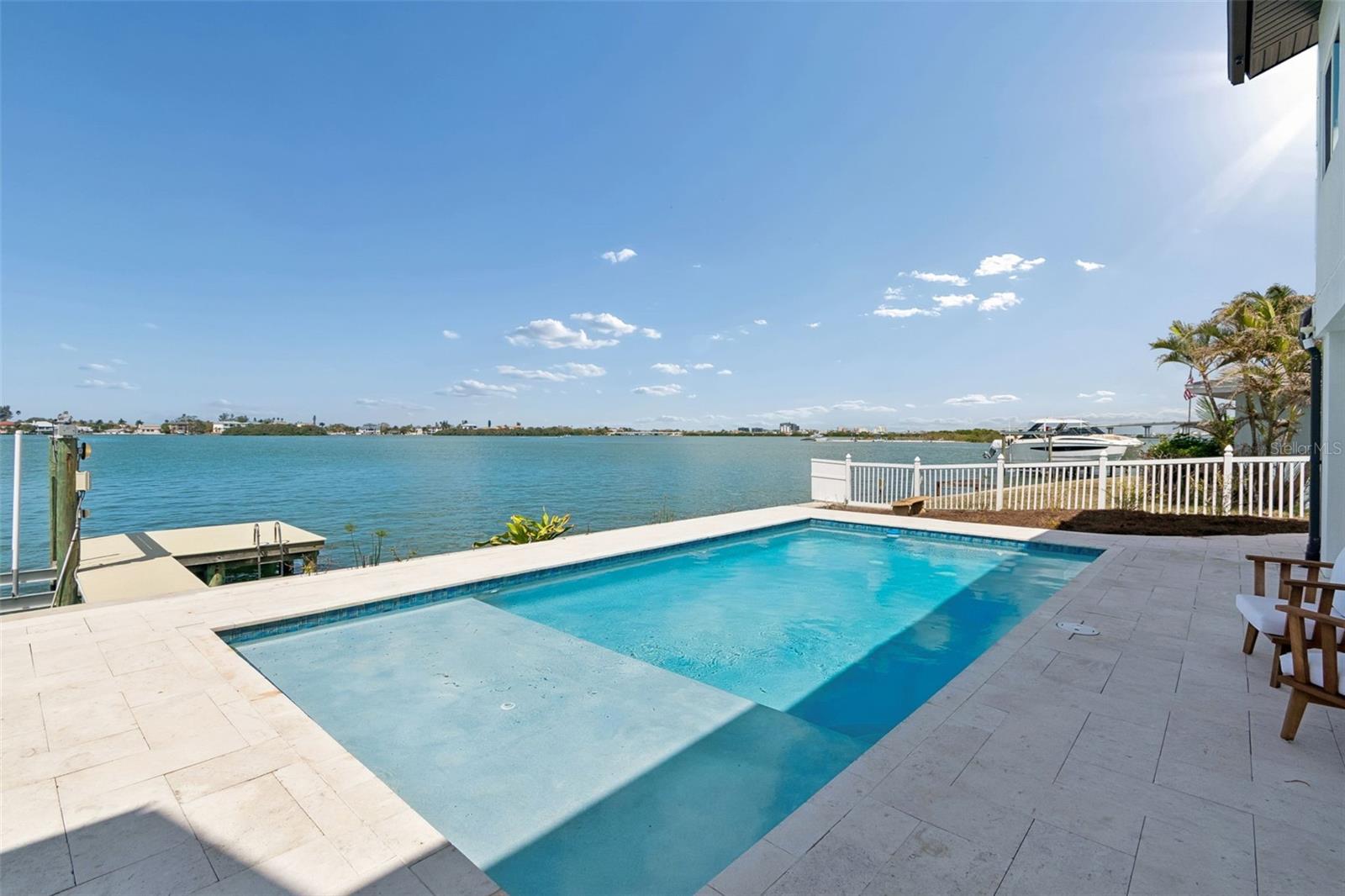 Waterfront pool with a shallow sun shelf overlooking the bay and a dock.