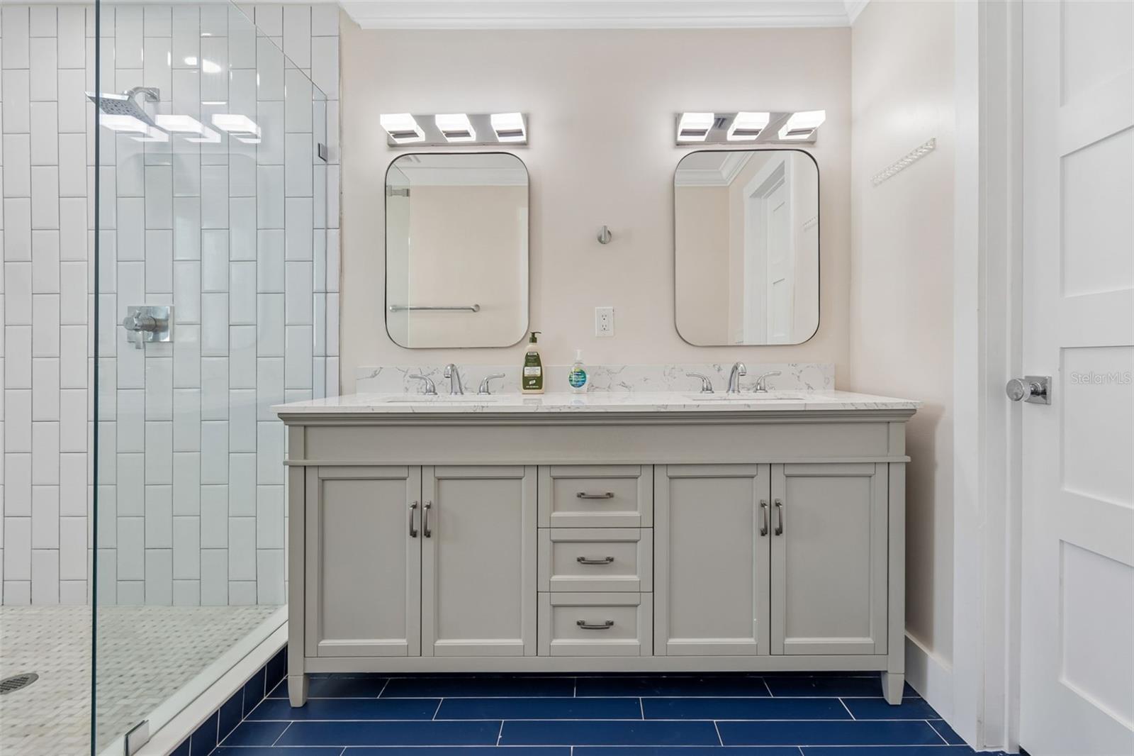 Bathroom with a gray double vanity, two mirrors, and a glass-enclosed tiled shower.